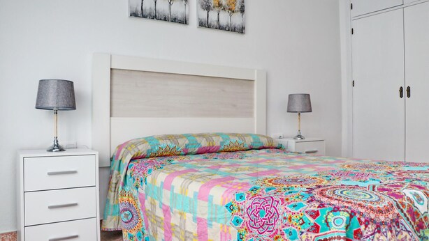 A bedroom with a bed, two bedside tables, a wardrobe, and two wall-mounted paintings.