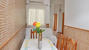 A small room with a brick wall, a white air conditioning unit, a table with a floral tablecloth, and a chair with a wooden headboard.