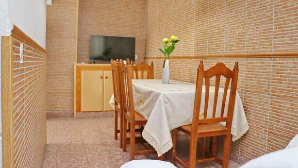 A dining area with a brick wall, a television on a wooden cabinet, and a table with chairs.