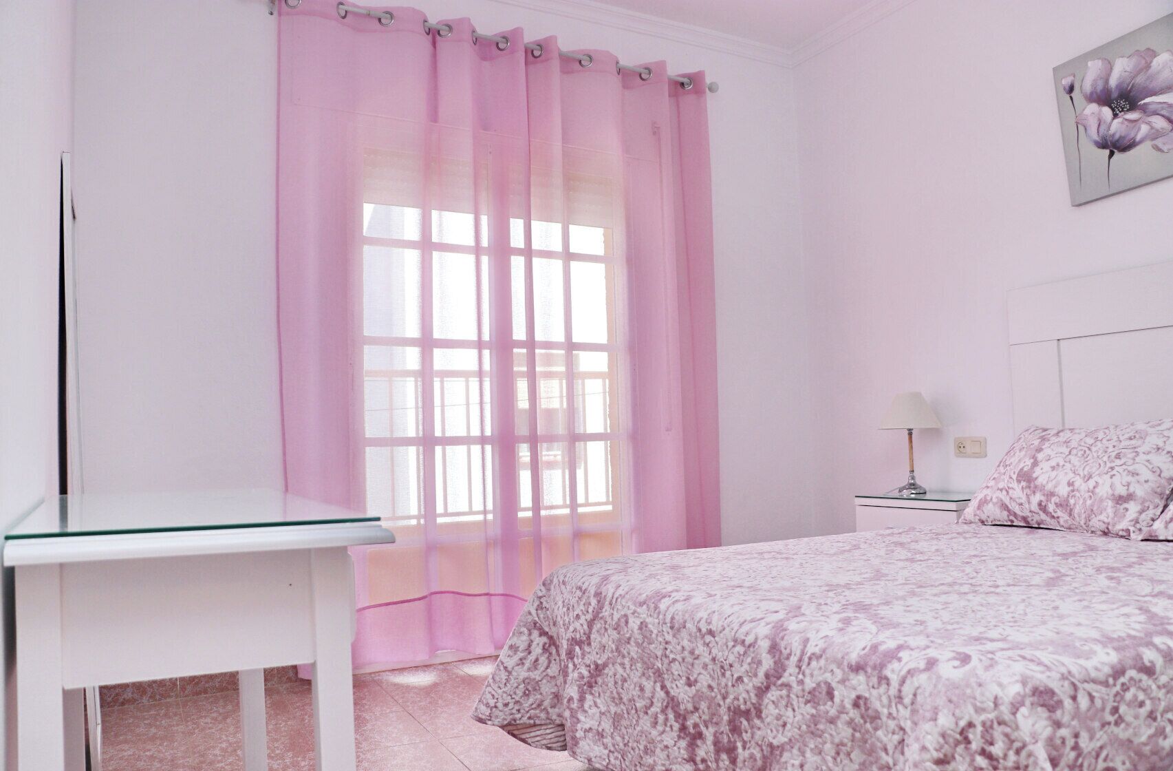 A bedroom with a bed, a bedside table, a lamp, and a window with curtains.