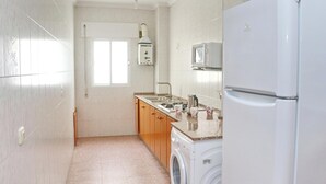 A compact kitchen with a washing machine, a microwave, and a refrigerator. - Apartment Violeta on the second floor (Conil de la Frontera)