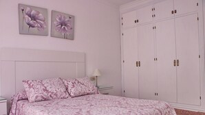 A bedroom with a bed, two wall-mounted floral paintings, a nightstand, a lamp, and a large wardrobe. - Apartment Violeta on the second floor (Conil de la Frontera)