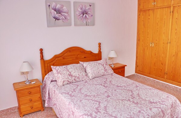 Cozy retreat with a wooden bed, nightstand, and wardrobe, adorned with patterned bedding and artwork.