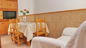 A small, cozy room with a dining table, two wooden chairs, a sofa, a TV, and a vase with flowers on the wall. - Apartment Violeta on the second floor (Conil de la Frontera)