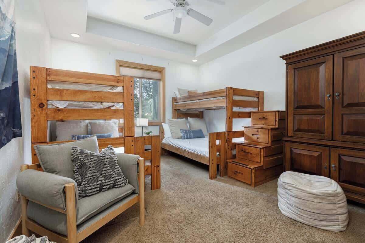 A cozy room with a bunk bed, a sofa, a cabinet, and a ceiling fan.