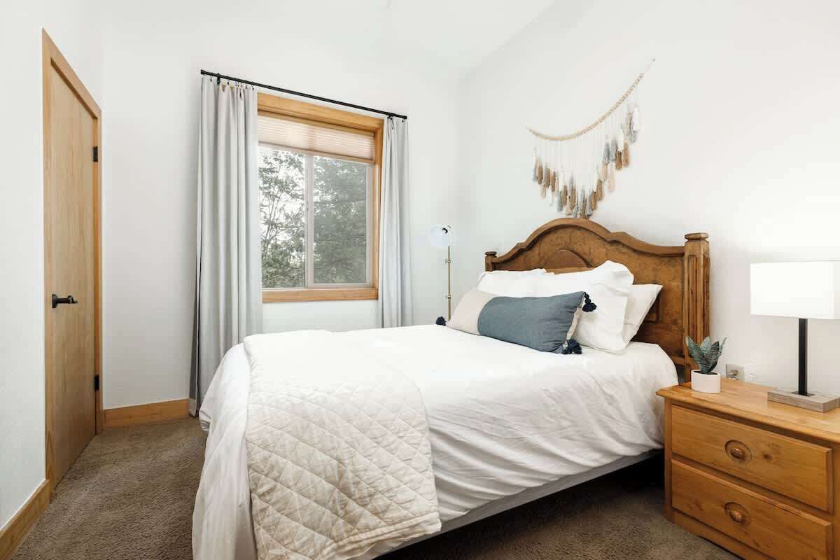 Un dormitorio con cama, mesita de noche, lámpara, ventana con cortinas y un adorno en la pared.