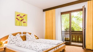 Una stanza con un letto, un comodino, un quadro, una finestra con tende e vista sul verde.