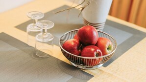 Un tavolo con una ciotola di metallo piena di mele rosse, un bicchiere e una pianta in vaso.