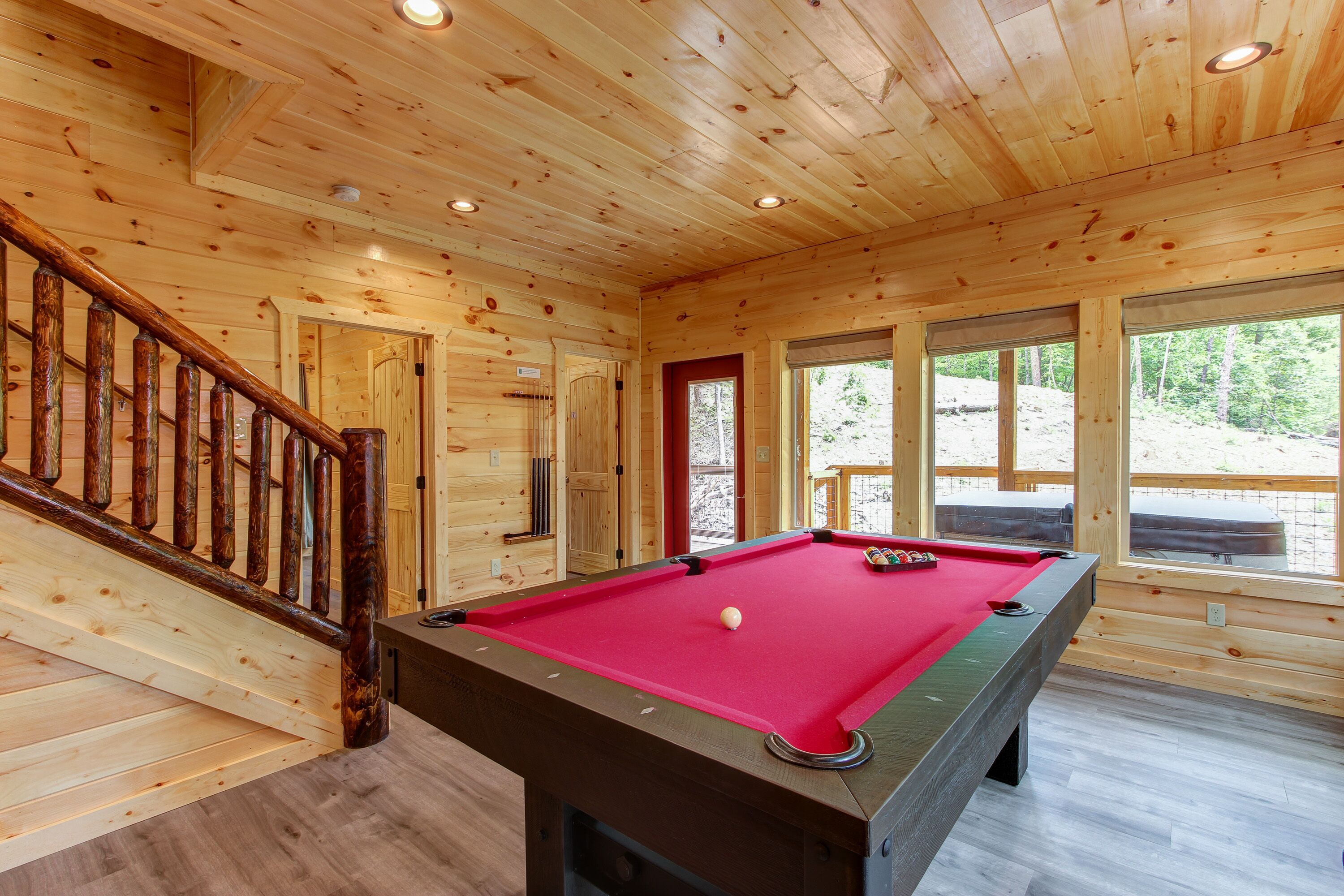 A wooden cabin with a pool table, wooden floors, and a staircase.