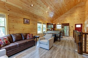 Un interior de cabaña espacioso con techo de madera, comedor, cocina con electrodomésticos modernos y una zona de estar acogedora con sofá y sillones de cuero.