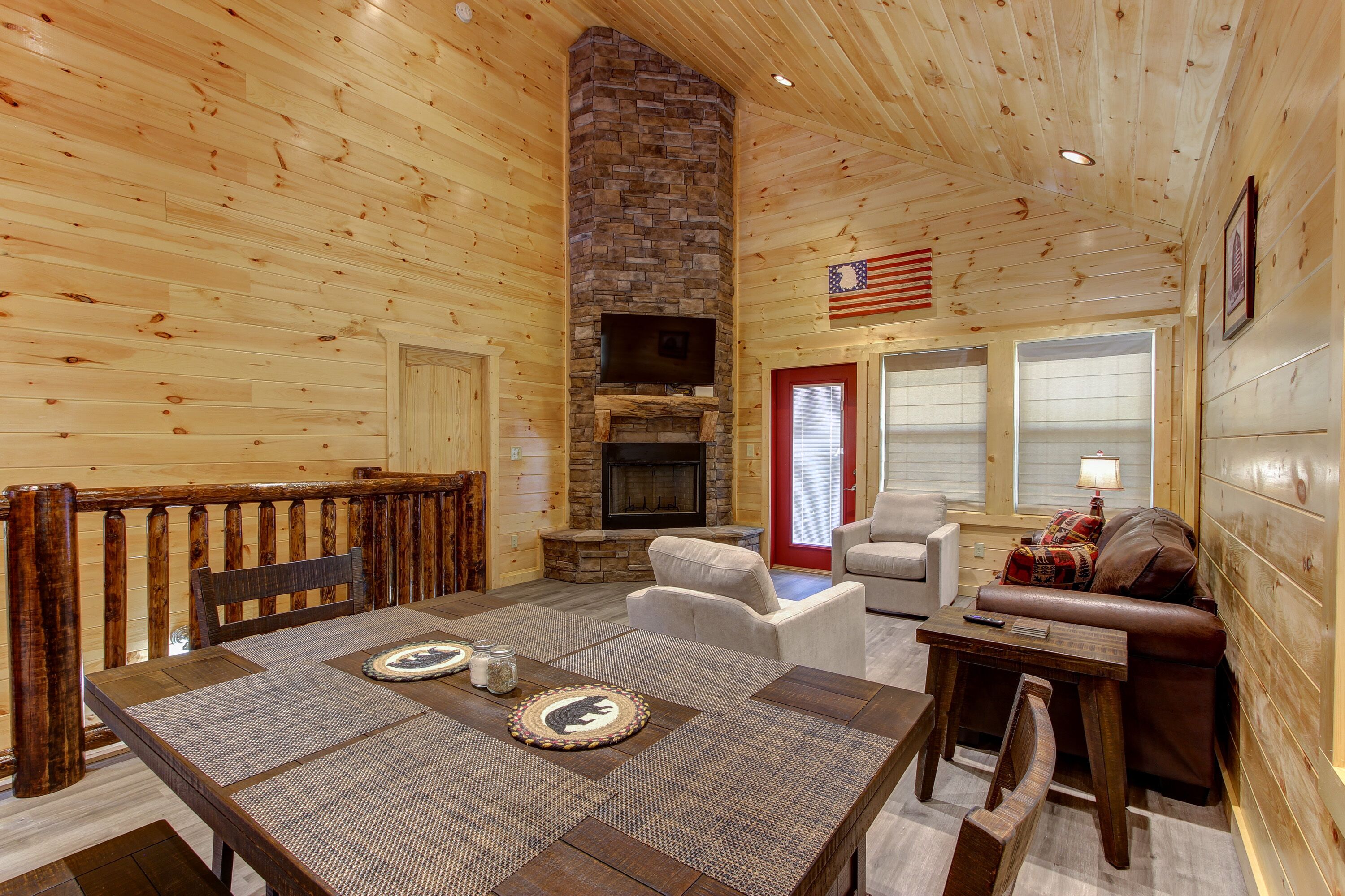Interior acogedor de una cabaña con chimenea de piedra, paredes de madera, una mesa de comedor con individuales y una zona de estar cómoda.