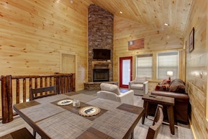 Interior acogedor de una cabaña con chimenea de piedra, paredes de madera, una mesa de comedor con individuales y una zona de estar cómoda.