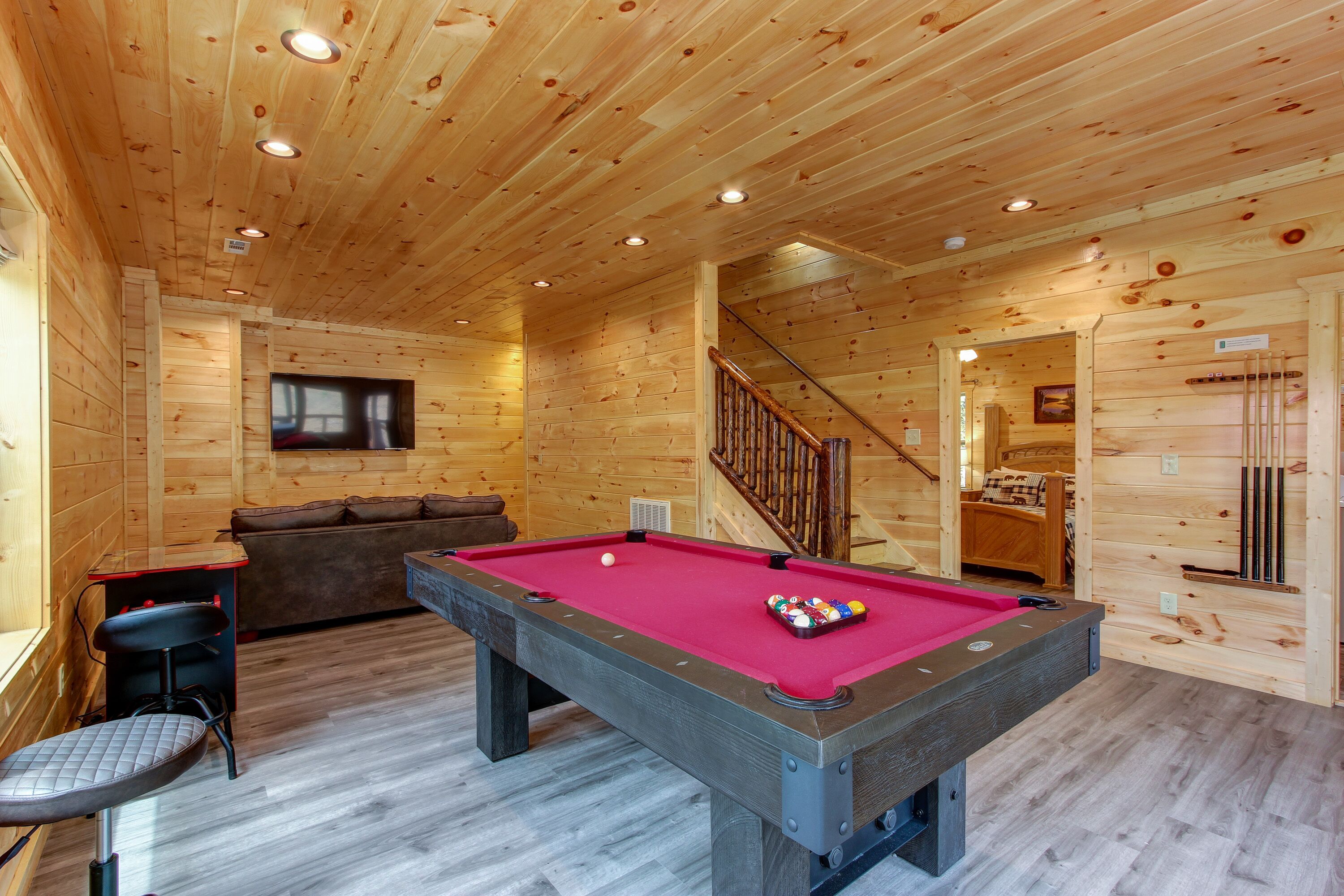 A wooden interior with a pool table, a sofa, and a staircase.