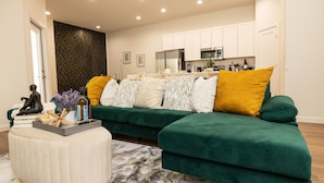 Un salon moderne avec un canapé vert, un pouf blanc et un tapis à motifs de marbre.