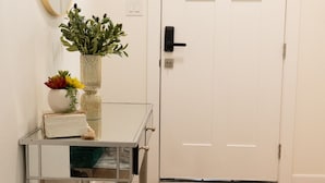 Un couloir avec une porte blanche, une petite table sur laquelle est posé un vase de fleurs et un miroir accroché au mur.