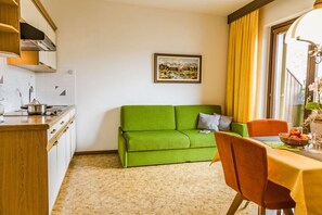 A compact living space with a kitchenette, a green sofa, a dining table with chairs, and a window with curtains. - Apartment 'Ferienwohnung Lanz 2' with Mountain View, Private Garden and Wi-Fi (Lana)