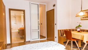 A bedroom with a bed, a shower, a dining area with a table and chairs, and a wooden door. - Studio Apartment 'Ferienwohnung Lanz 3' with Mountain View, Private Garden and Wi-Fi (Lana)