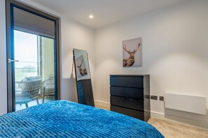 A bedroom with a bed, a dresser, a painting of a deer, and a balcony with chairs.