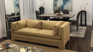 Ett modernt vardagsrum med en beige soffa, ett soffbord i glas och en matplats med ett bord och stolar i trä.