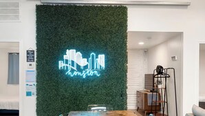 Una sala de conferencias con una mesa de madera, sillas, un letrero luminoso con un paisaje urbano y una pared verde.