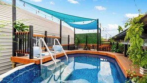 Una piscina con muelle de madera y zona sombreada.