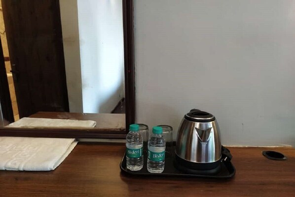 A wooden tray with two Bisleri water bottles and a stainless steel kettle on a hotel room table.