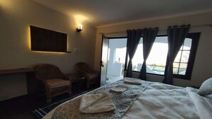 A hotel room with a bed, two chairs, a table, a wall-mounted light, and a window with curtains. - Kumaon Roop Resort (Kosiyakutoli)