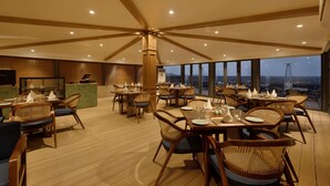 A restaurant with wooden flooring, wicker chairs, and tables set for dining. - Sarovar Portico Srinagar (Budgam)
