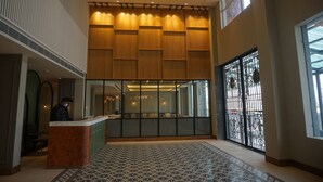 A hotel lobby with a reception desk, a patterned carpet, a large window with a view, and a modern ceiling design. - Sarovar Portico Srinagar (Budgam)