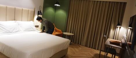 A hotel room with a large bed, a small round table, a chair, a desk with a chair, and a green accent wall.