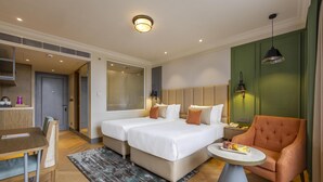 A hotel room with two beds, a dining table, a chair, a small table with fruit, and a green accent wall. - Sarovar Portico Srinagar (Budgam)