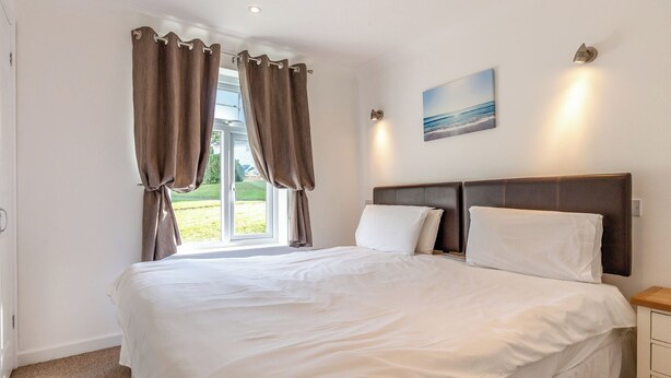 Een slaapkamer met een groot bed, een raam met gordijnen, een nachtkastje en een wandlamp.