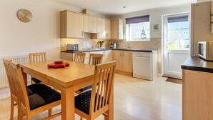 Een moderne keuken met houten kastjes, een eettafel met stoelen, een inbouw vaatwasser en een magnetron.