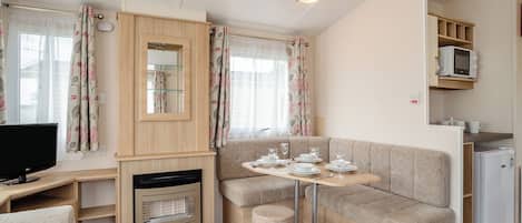 Un espacio habitable compacto con kitchenette, un sofá, una pequeña mesa lista para comer y un televisor.