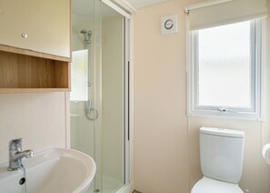 A bathroom with a glass-enclosed shower, a toilet, a sink, and a window.