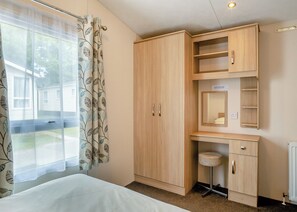 A bedroom with a bed, a wardrobe, a desk with a chair, and a window with curtains.