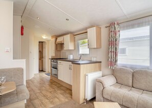 A compact kitchenette with a stove, oven, and sink, a sofa, and a window with curtains.