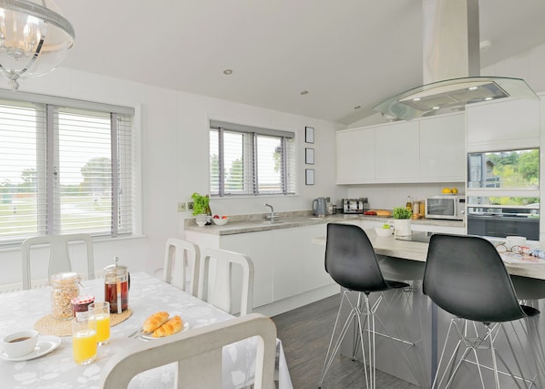 A modern kitchen with white cabinetry, a dining table with chairs, and a breakfast setup. - 3 bedroom accommodation in Bury St Edmunds (Bury St Edmunds)