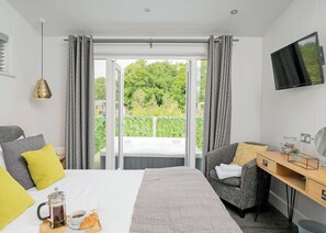 Habitación de hotel con cama, escritorio, silla, televisión y balcón con vistas a zonas verdes.