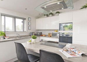 Une cuisine moderne avec des meubles blancs, un four encastré et une fenêtre équipée de stores.