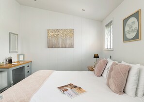 Une chambre à coucher comprenant un lit, une table de chevet, une lampe, un tableau encadré et une œuvre d’art murale.