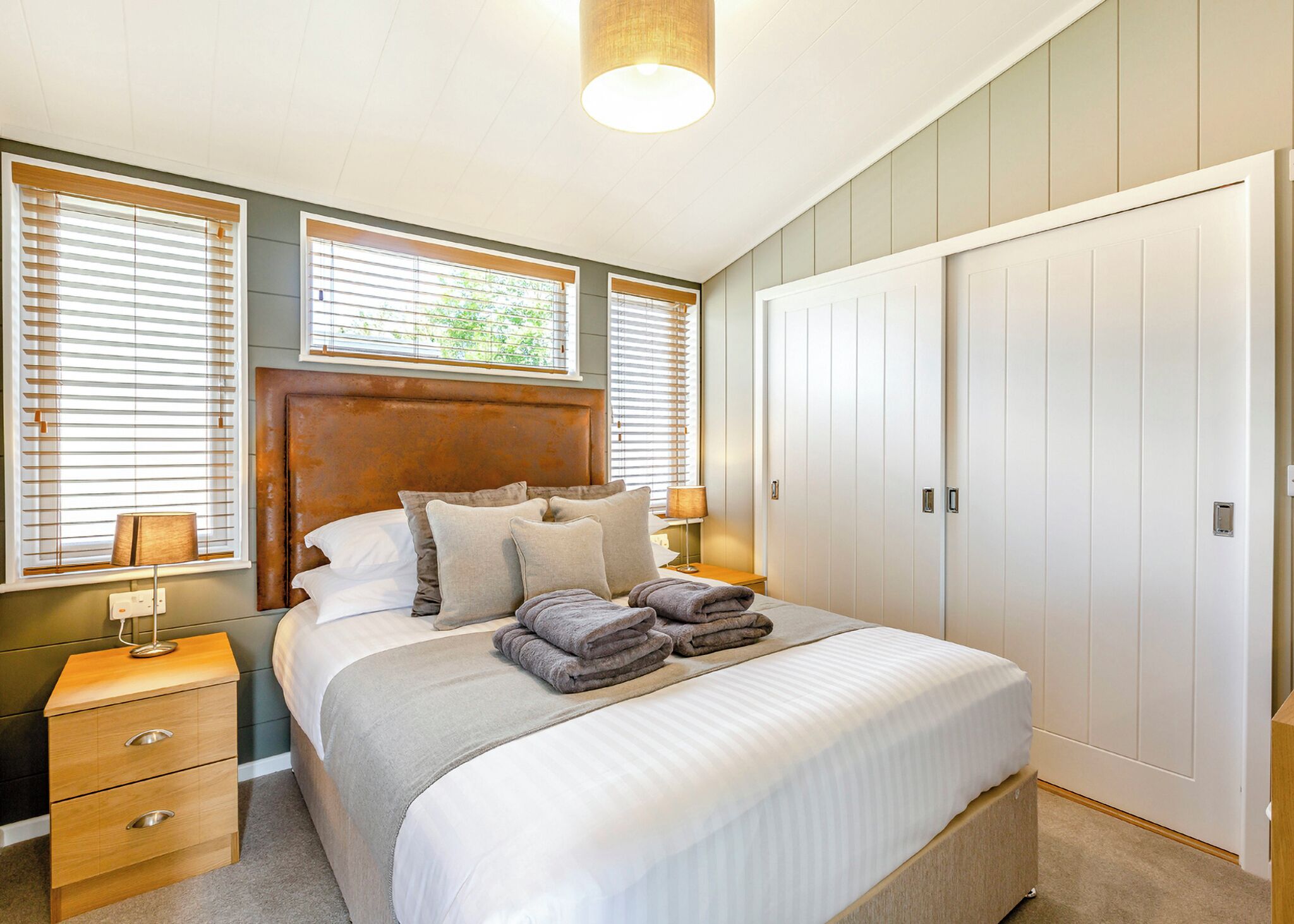 Une chambre à coucher comprenant un lit, des tables de chevet, une armoire et des fenêtres équipées de stores.