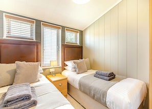 A bedroom with two beds, a nightstand, and a window with blinds.