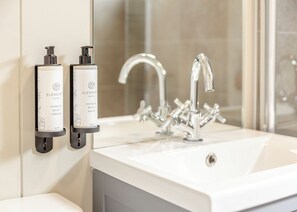 A bathroom with a white sink, a modern faucet, and two hand and body wash dispensers mounted on the wall.