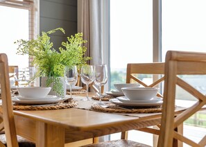 Una mesa de comedor dispuesta con platos, cazuelas y copas de vino blancos, junto con una pequeña planta verde.