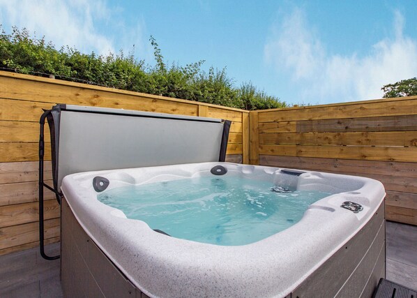 A hot tub with a wooden deck and a wooden fence in the background.