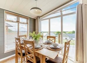 Un comedor con una mesa dispuesta para cuatro, ventanas amplias y vistas al campo.