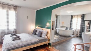 A modern hotel room with a wooden bed, a large mirror, a bathtub, and a separate shower area. - Villa within walking distance of Flayosc (Flayosc)