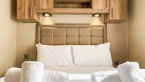 A hotel room with a bed, white towels, wooden cabinets, and a light fixture above the bed.