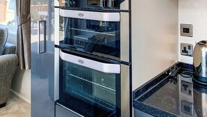 A modern kitchen with a double oven, a stainless steel range hood, and a black countertop.